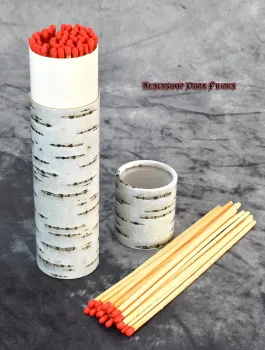 Hexenshop Dark Phönix Ein 20 cm langes Streichholz entzündet eine tiefe Ritualglaskerze, dekorative Baumrinden-Verpackung im Hintergrund.