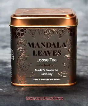 Kupferfarbene, kunstvoll verzierte Teedose von Mandala Leaves mit dem Etikett „Merlin’s Lieblings Earl Grey“ vor dunklem Hintergrund.